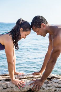 Vertical close-up of Young couple on beach, facing each other in Cow yoga pose with water in background