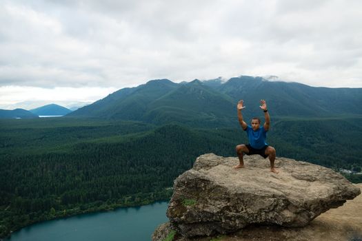 Young man in yoga pose on top of mountain with beautiful vista in background.