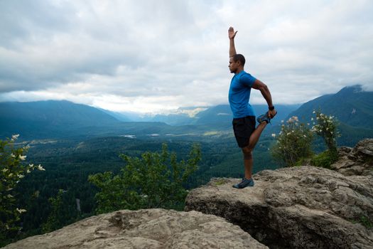 Young man in yoga pose on top of mountain with beautiful vista in background.