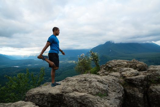 Young man in yoga pose on top of mountain with beautiful vista in background.