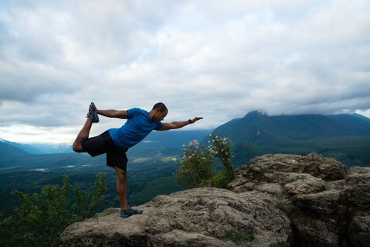 Young man in yoga pose on top of mountain with beautiful vista in background.