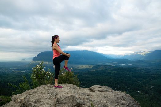 Young woman in yoga pose on top of mountain with beautiful vista in background.