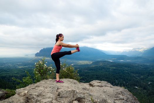 Young woman in yoga pose on top of mountain with beautiful vista in background.