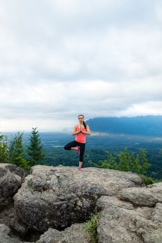 Young woman in yoga pose on top of mountain with beautiful vista in background.