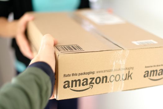 STUTTGART - SEPTEMBER 2: Woman receiving a parcel by Amazon.com delivered by the mailman in front of her flat on September 2, 2012 in Stuttgart, Germany. Amazon.com is delivering thousands of parcels every day to German households.
