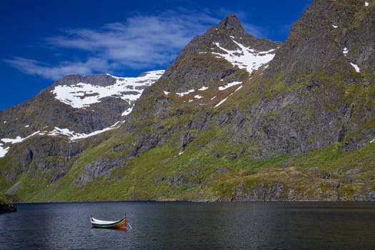Canoe in fjord surrounded by towering mountain peaks with patches of snow