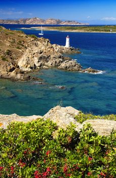 Lighthouse on Sardinian rocks and a yacht sailing in the sea