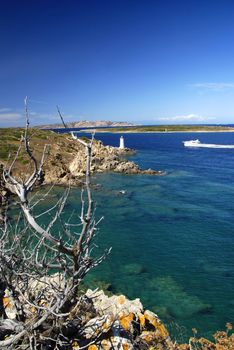 Lighthouse on Sardinian rocks and a yacht sailing in the sea