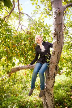 Girl sitting on a apple tree smiling at the camera