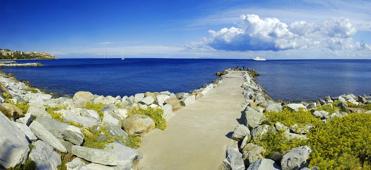 Long stone pier on Corsica with a luxury yacht in the back and dramatic sky above - wide panorama