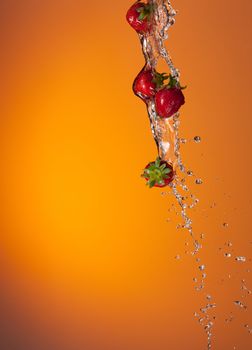 water splash with ripe red strawberry over orange background