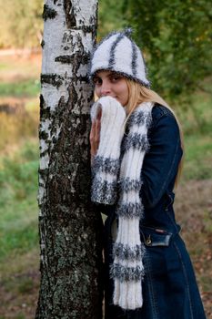 A standing girl in a cup and scarf and jeans coat in a forest
