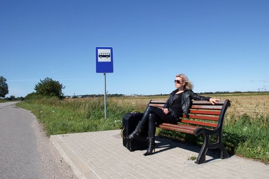 lonely woman sitting on a bench at a bus stop in the countryside
