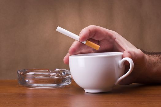 Hand holding a cigarette and a cup ashtray.