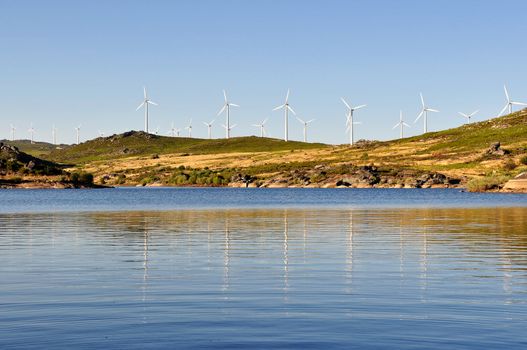 Wind mill, with several wind turbines, near a river, producing green energy.