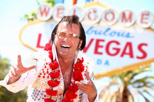 Las Vegas Elvis impersonator laughing having fun in front of Welcome to Fabulous Las Vegas sign.