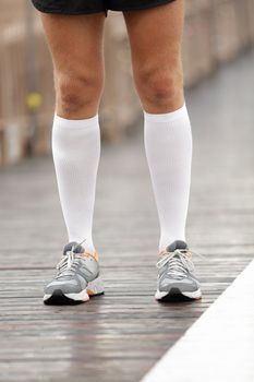 Running shoes and compression socks on male runner. Closeup of runners feet on Brooklyn Bridge, New York City.