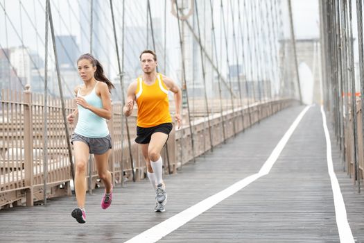 Running couple. Runners training outside. Asian woman and Caucasian man runner and fitness sport models jogging in full body showing Brooklyn Bridge, New York City, USA.
