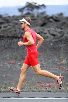 Triathlon runner man. Triathlete running training on Hawaii for ironman. Male athlete running in red compression clothing, shorts and top on volcano on Big Island, Hawaii.