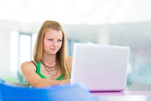 pretty female college student working on her laptop computer on campus, before class (color toned image; shallow DOF)