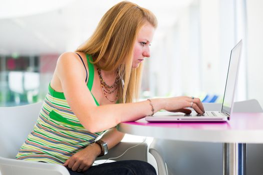 pretty female college student working on her laptop computer on campus, before class (color toned image; shallow DOF)