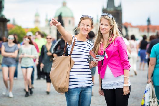 Two female tourists walking along the Charles Bridge while sightseeing in Prague, the historical capital of the Czech Republic (color toned image; shallow DOF)