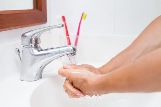 Washing hands under running water in a bathroom (shallow DOF; color toned image)