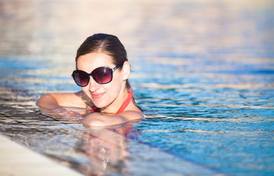 Portrait of a young woman relaxing in a swimming pool (shallow DOF; color toned image)