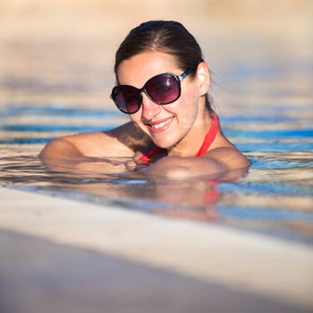 Portrait of a young woman relaxing in a swimming pool (shallow DOF; color toned image)