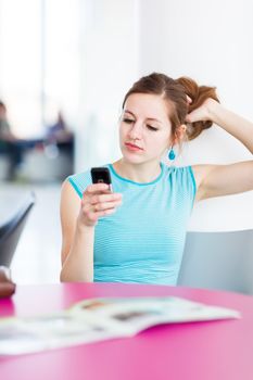 Pretty young woman using her mobile phone/speaking on the phone in a public area (shallow DOF; color toned image)