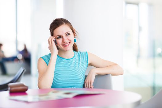 Pretty young woman using her mobile phone/speaking on the phone in a public area (shallow DOF; color toned image)