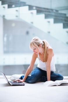 On campus - pretty female student with laptop and books working before class on her assignment/homework  (color toned image)