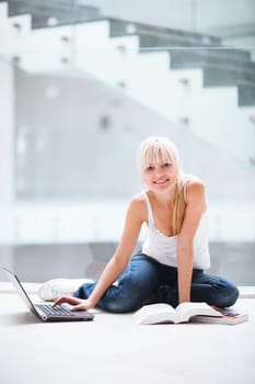 On campus - pretty female student with laptop and books working before class on her assignment/homework  (color toned image)