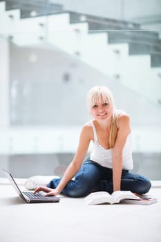 On campus - pretty female student with laptop and books working before class on her assignment/homework  (color toned image)