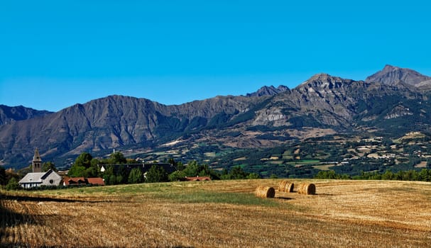 Beautiful landscape with a filed and a village near big mountains in The Alps, in France.