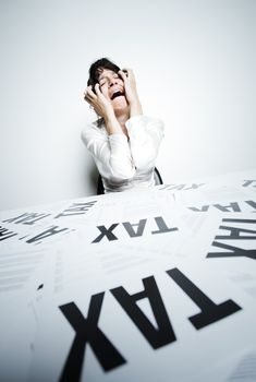 Desperate woman at her taxes-paperwork covered desk to crying bitter tears with her hands on face