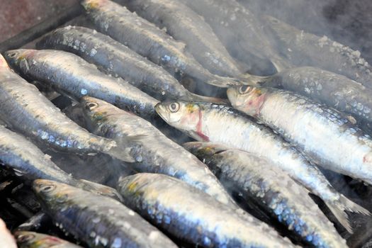 Fresh sardines being grilled in a charcoal grill with smoke around