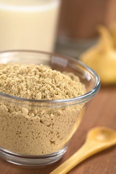 Powdered Maca or Peruvian ginseng (lat. Lepidium meyenii) in glass bowl with milk, chocolate drink and maca roots in the back (Selective Focus, Focus one third into the maca powder)