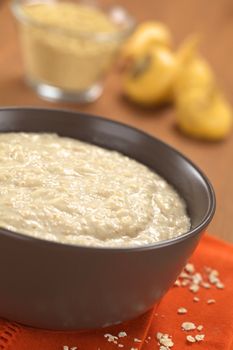 Bowl of cooked oatmeal porridge mixed with powdered maca or Peruvian ginseng (lat. Lepidium meyenii) with maca roots and maca powder in the back (Selective Focus, Focus in the middle of the oatmeal porridge) 