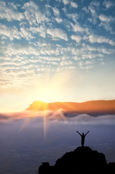 A man standing at mountain top with open arms set against a beautiful sunrise