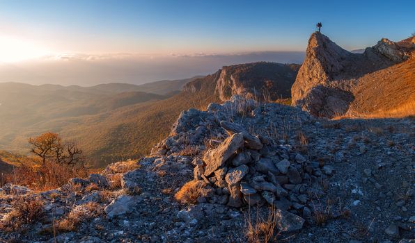 A man standing at mountain top with camera against a beautiful sunrise