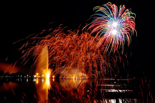 Impressive, bright and colorful fireworks over a lake with lighten water fountain, great celebration background.