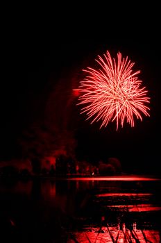 Beautiful red firework over a lake with reflections, perfect black sky as copy space for text.