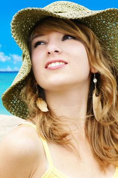 Portrait of a beautiful young blond woman on vacations at the beach with large straw sun hat.
