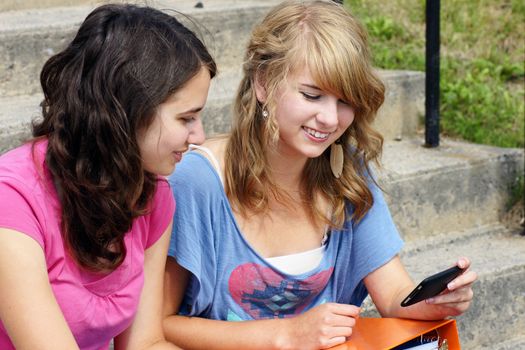 Two young teenager students using their cell phone and laughing, perfect for networking, social media and the likes.