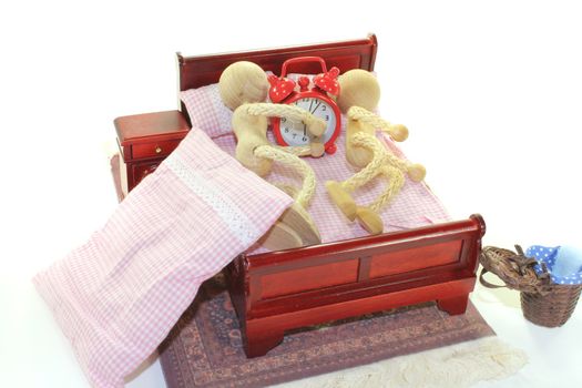 Sleep - two wooden doll and alarm clock in bed with bedside table and plaid bedding