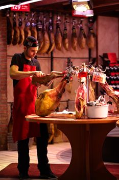 BARCELONA - MAY 21: Young man, a jamon seller, in a robe and cap is cutting meat in the supermarket on May 21, 2012 in Barcelona, Spain.