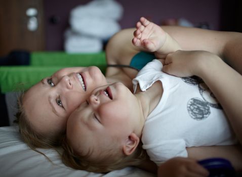 Happy young mother with a 1,5-year-old baby are embracing and relaxing on the bed of a hotel room