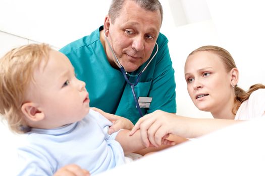 A middle-aged doctor is listening to a baby’s back with a stethoscope in  a medical study. The baby is 16 months old. The young mother is looking at her son with alarm. Caucasian. Focus on the mother and on the doctor.