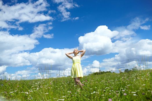 A girl in a yellow dress is lying in the sun in the field with meadow flowers.